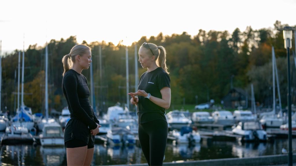 Løpecoach gir individuell veiledning til løper ved marina i solnedgang.