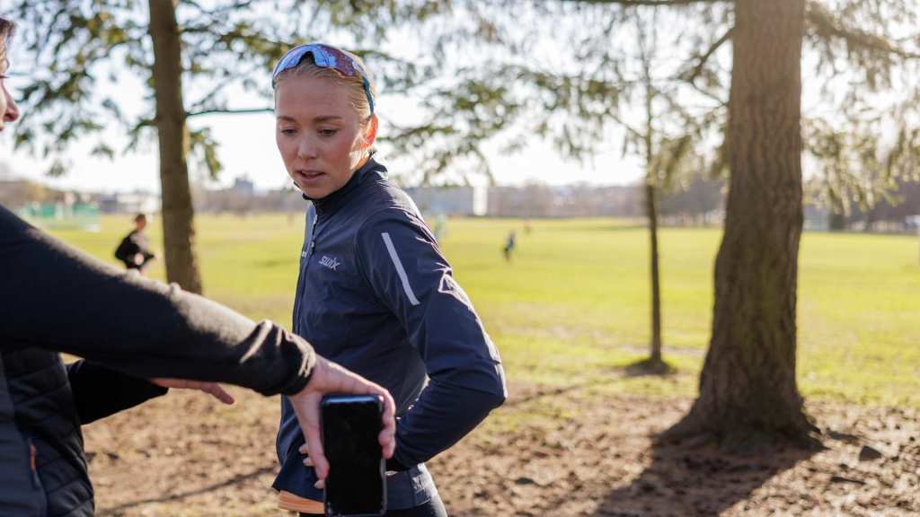 Løper får veiledning om løpefart og pace ved hjelp av mobil og klokke under trening i parkområde